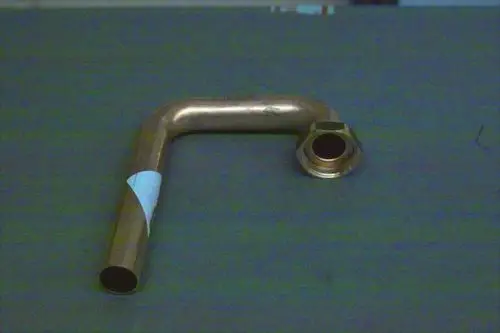 Brötje Vorlaufrohr mit einem gebogenen Ende und Anschluss zum Schrauben. Das Rohr hat eine metallische Oberfläche und liegt auf einer grauen Fläche.