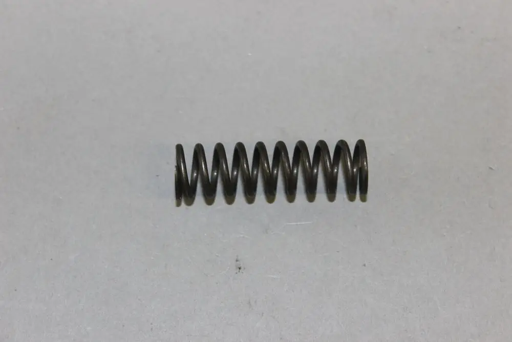 Schwarze Druckfeder, spiralförmig gewickelt, auf grauem Hintergrund. Teil einer Brötje-Anlage, möglicherweise für eine Stellschraube.