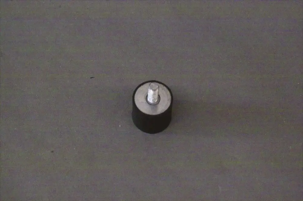 Schwarzer Schwingungsdämpfer mit silbernem Oberteil und Gewinde, abgestellt auf einer grauen Fläche. Produkt von Brötje.