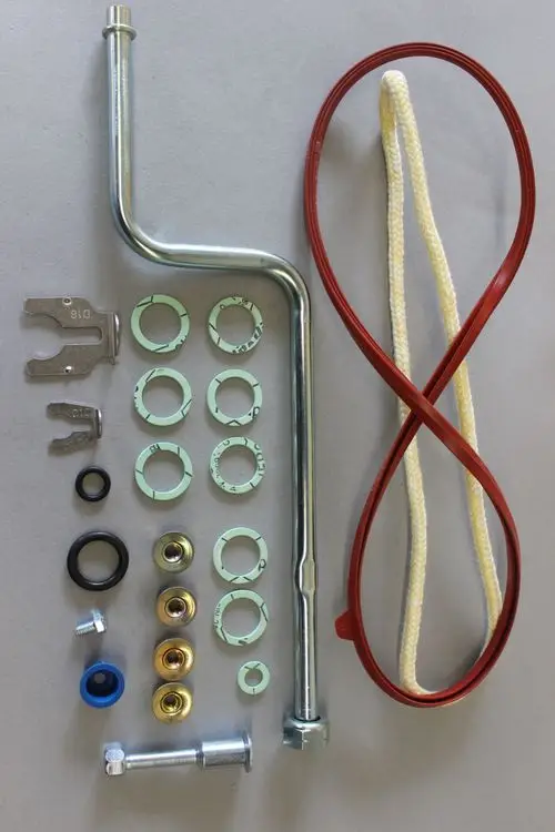 Brötje Zubehörteil, bestehend aus verschiedenen Rohren, Unterlegscheiben, Dichtungen und einem Kabel. Teile sind auf grauem Hintergrund angeordnet.