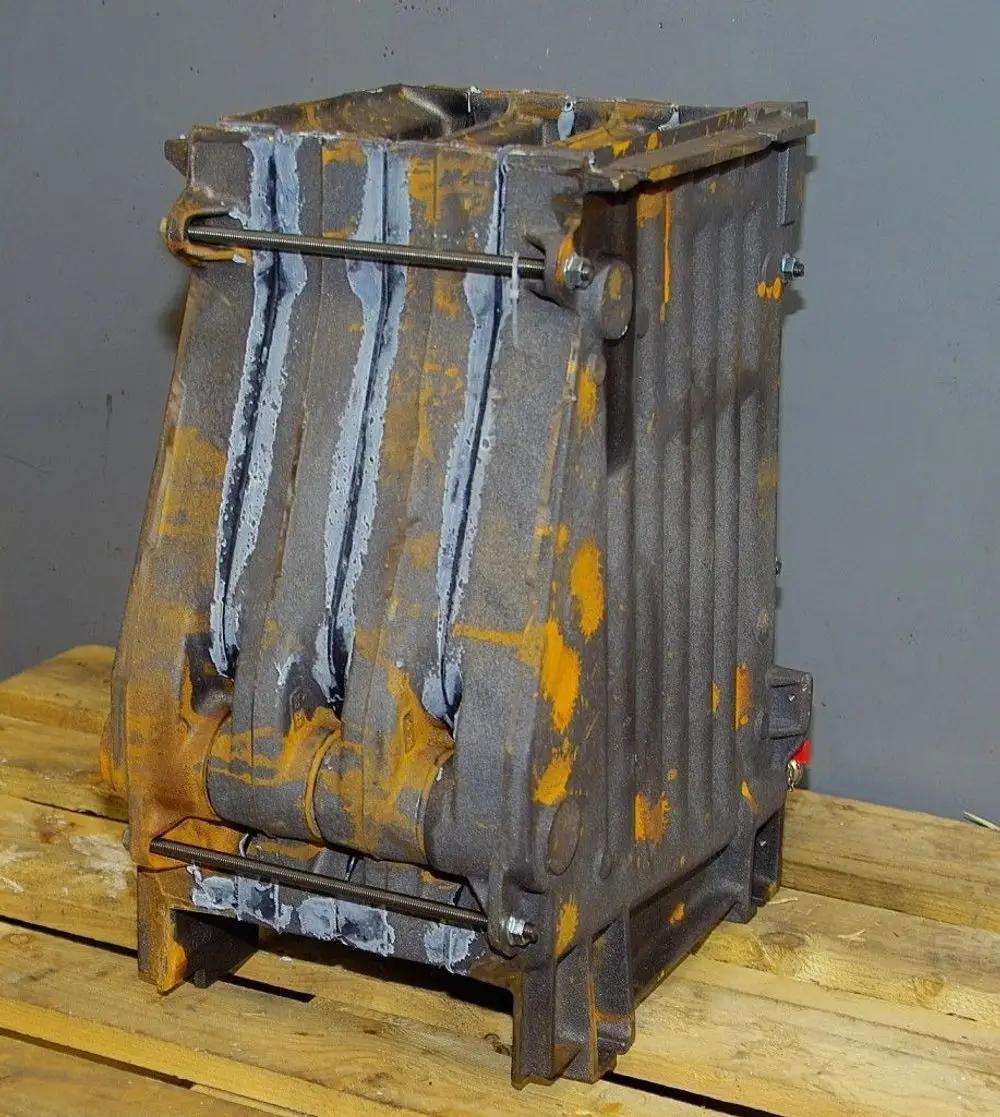 Brötje Kesselblock in rechteckiger Form, aus metallischem Material, mit mehreren horizontalen Kanälen und einem Stahlstab an der Vorderseite, auf Holzpaletten platziert.