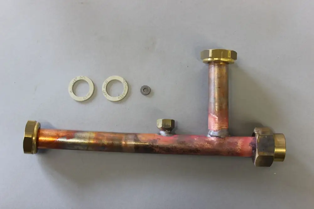 Brötje Vorlaufverteiler aus Kupfer mit mehreren Fittings und Dichtungen, auf grauem Untergrund. Enthält zwei Dichtungen und eine kleine Unterlegscheibe.