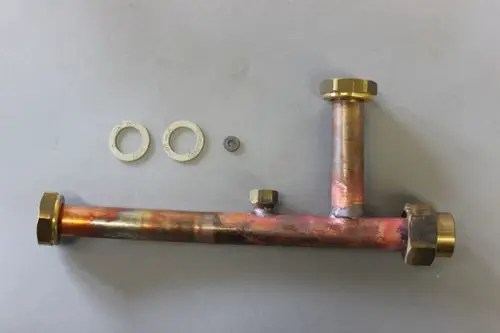 Brötje Vorlaufverteiler aus Kupfer mit mehreren Fittings und Dichtungen, auf grauem Untergrund. Enthält zwei Dichtungen und eine kleine Unterlegscheibe.