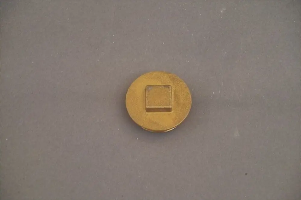 Runder Metallstopfen mit quadratischem Präger, auf grauem Untergrund, möglicherweise von der Marke Brötje.