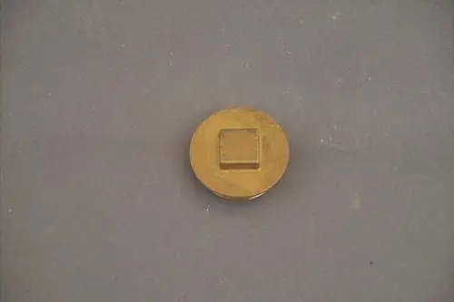 Runder Metallstopfen mit quadratischem Präger, auf grauem Untergrund, möglicherweise von der Marke Brötje.