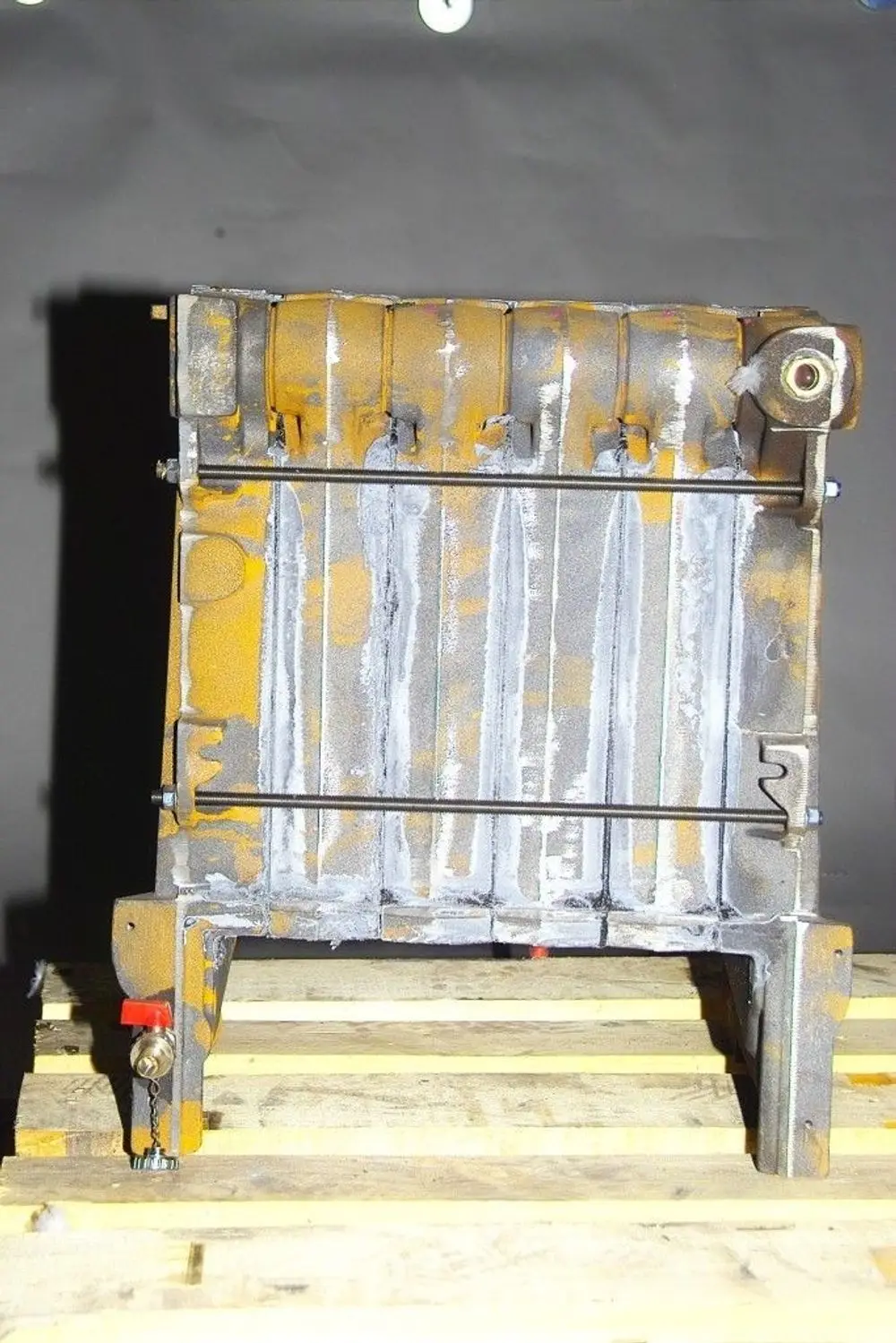 Brötje Kesselblock in grauer Farbe, auf einer Holzpalette platziert. Sichtbare Verbindungsstücke und Mechanismen an der Unterseite.