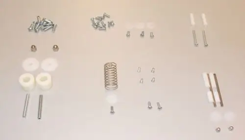 Brötje Kleinteile Set mit verschiedenen Schrauben, Unterlegscheiben, Stiften, einer Feder und Kunststoffteilen auf einer weißen Unterlage angeordnet.