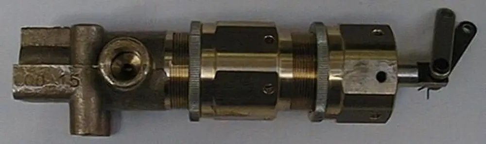 Druckkolben von Brötje, mit metallischer Oberfläche, besteht aus mehreren zylindrischen und quadratischen Elementen, hat eine seitliche Öffnung und eine bewegliche Klappe.
