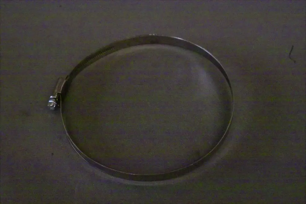 Brötje Schlauchschelle aus Metall, rund geformt, mit einem Spannmechanismus auf einer dunklen Unterlage.