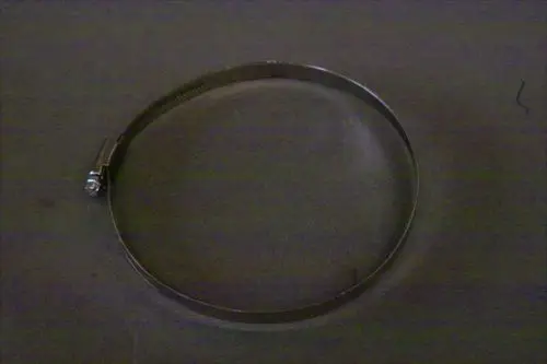 Brötje Schlauchschelle aus Metall, rund geformt, mit einem Spannmechanismus auf einer dunklen Unterlage.