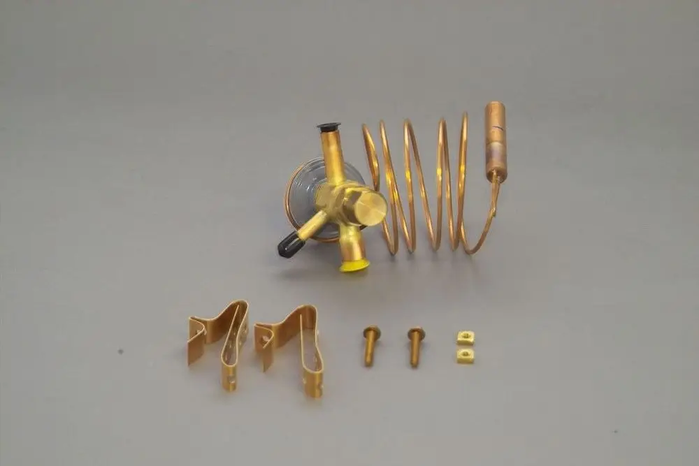 Brötje Expansionsventil in goldener Farbe mit spiralisiertem Rohr und Befestigungsteilen, auf grauem Hintergrund angeordnet.