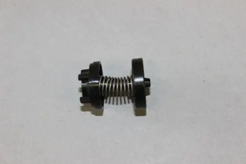 Black spring-loaded component with circular ends, likely part of a Brötje heating system, positioned on a light gray surface.