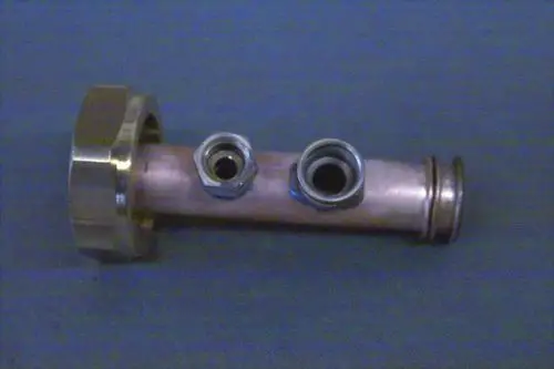 Brötje Heizungsrücklaufleitung aus Metall mit drei Anschlussmöglichkeiten, einer größeren und zwei kleineren Öffnungen, auf grauem Hintergrund.