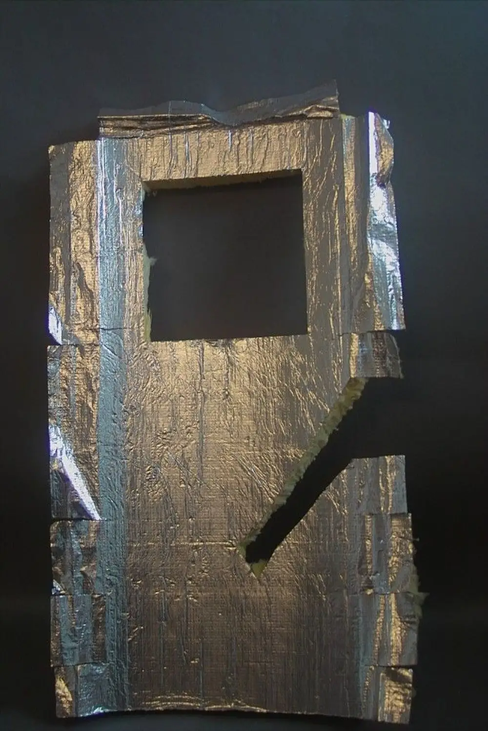 Silberne Isolationsmatte mit rechteckigem Fenster und unregelmäßigen Kanten. Die Oberfläche wirkt reflektierend und ist an mehreren Stellen bearbeitet. Hersteller ist Brötje.