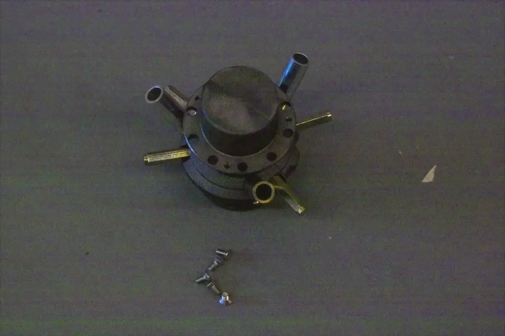 Gasverteiler von Brötje mit mehreren Anschlussleitungen und einer Grundlage für Montage, auf einem grauen Untergrund platziert. Schrauben liegen daneben.