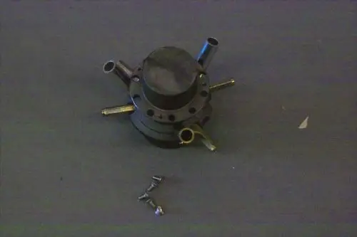 Gasverteiler von Brötje mit mehreren Anschlussleitungen und einer Grundlage für Montage, auf einem grauen Untergrund platziert. Schrauben liegen daneben.