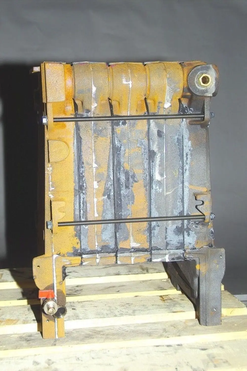 Brötje Kesselblock in dunkelgrauer Farbe, mit mehreren Längskanälen und sichtbarem Befestigungsmechanismus, auf Holzpalette platziert.