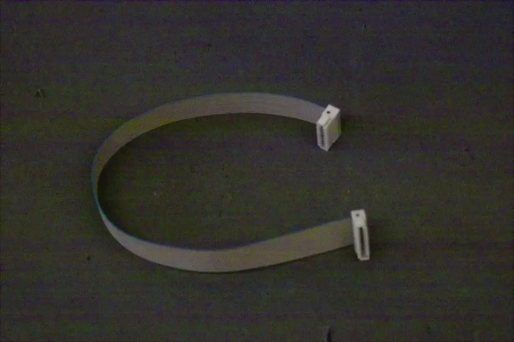 Weißes Flachbandkabel mit zwei Steckern an den Enden, auf dunklem Untergrund liegend. Teil eines Brötje Busmoduls zur Datenkommunikation.