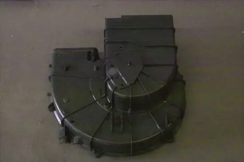 Schwarzes Ansauggehäuse von Brötje, mit mehreren Anschlussöffnungen und einer strukturierten Oberfläche. Das Gehäuse ist flach und hat eine asymmetrische Form.