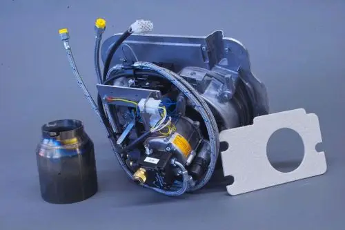 Brötje-Brenner aus Metall mit angeschlossenen Leitungen und einer Halterung, komplett mit einem runden Bauteil und Dichtungsplatte auf grauem Hintergrund.