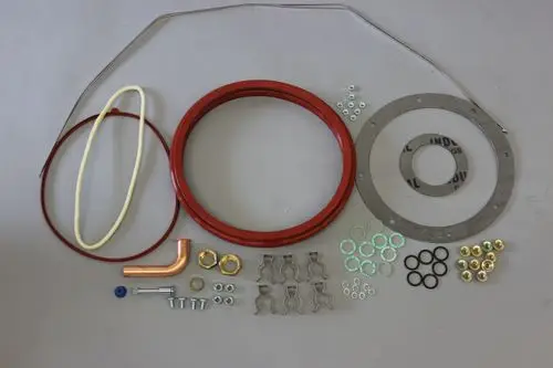 Brötje Dichtungen und Zubehörteile für einen Stirling-Motor, einschließlich Ringe, Schrauben, Unterlegscheiben und Kupferrohr, auf glattem Untergrund angeordnet.