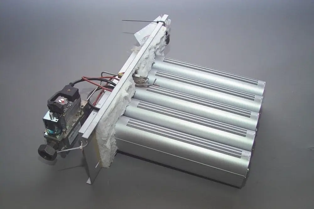 Brötje Heizgerät mit mehreren silbernen Rohren und einer Baugruppe, die elektrische und parametrierbare Komponenten beinhaltet, auf grauem Hintergrund.