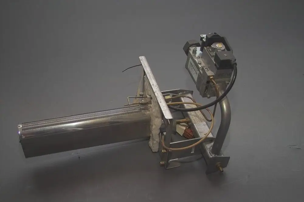 Brötje Brenner mit metallischem Gehäuse und verbundenen Leitungen. Die Baugruppe umfasst einen Brennerkopf und Regelmechanismus ohne sichtbare Montageelemente.