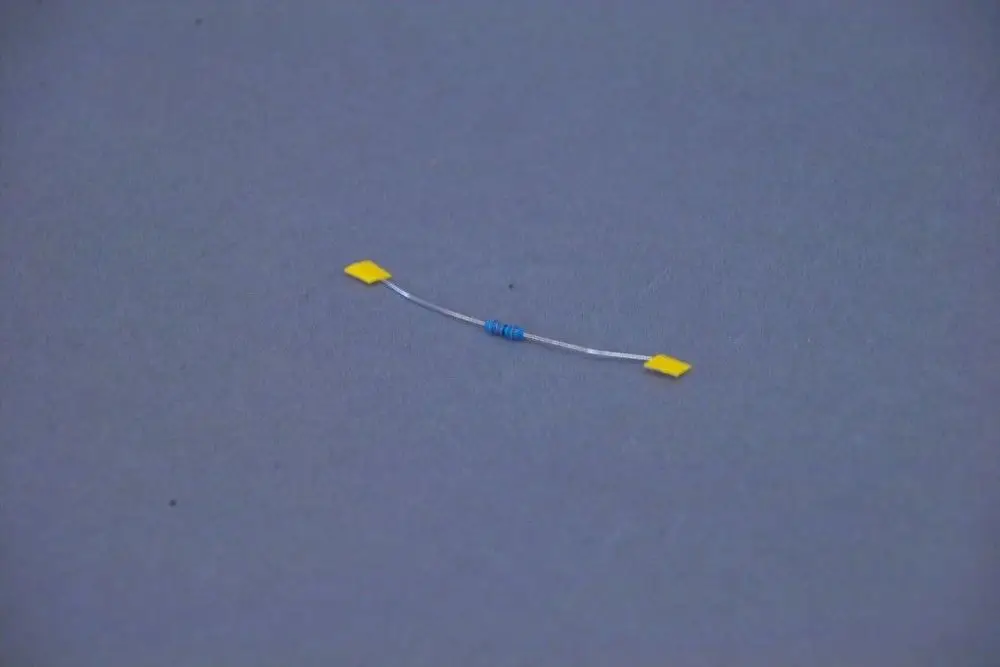 Brötje Widerstand mit blauer Wicklung und gelben Anschlussflächen, auf grauem Hintergrund.