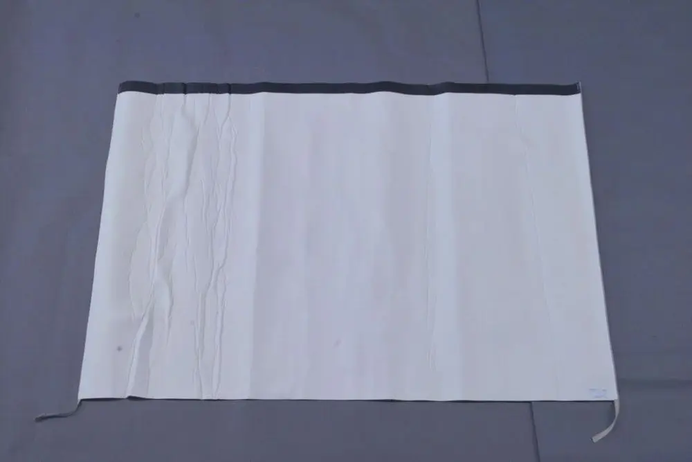 Brötje Folienmantel in weißer Ausführung, flach und ohne erkennbare Maße, auf grauem Untergrund ausgebreitet. Detaillierte Faltungen und eine schwarze Oberkante sind sichtbar.