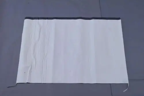 Brötje Folienmantel in weißer Ausführung, flach und ohne erkennbare Maße, auf grauem Untergrund ausgebreitet. Detaillierte Faltungen und eine schwarze Oberkante sind sichtbar.