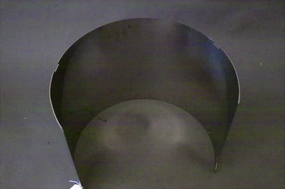 Schwarze, halbrunde Metallfläche mit offenen Kanten, welche möglicherweise Bestandteil eines Brennraums von Brötje ist. Hintergrund in dunkler Farbe.