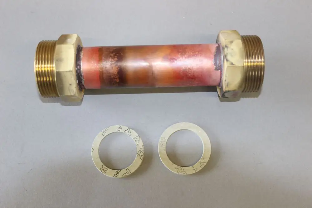 Brötje-Pumpenersatzrohr aus Kupfer mit zwei Gewindemuffen an den Enden. Daneben zwei Dichtscheiben aus Metall.