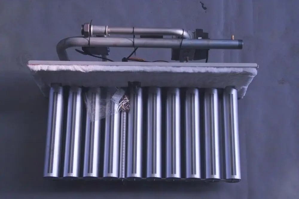 Brötje Brenner aus Metall mit mehreren Zylindern und einer oberhalb montierten Rohrleitung, auf einer weichen Unterlage platziert, vor neutralem Hintergrund.