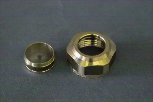 Brötje Verschraubungs-Set mit zwei Metallteilen, einem größeren, sechseckigen und einem kleineren, runden Element, auf einer grauen Oberfläche platziert.