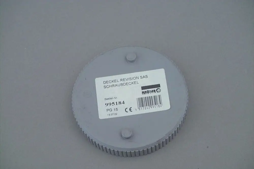 Grauer runder Deckel mit Schraubmechanismus und Etikett. Auf der Oberfläche sind diese Details zu sehen: Produktnummer, Barcode und Sicherheitszeichen. Markierung für Brötje.