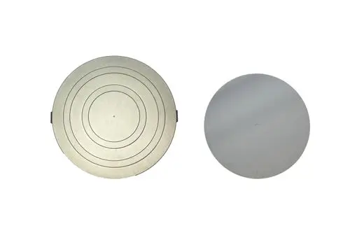 Zwei runde Metalldeckel, einer mit konzentrischen Kreisen und seitlicher Halterung, der andere glatt und ohne Zusatz. Brötje Isolierung möglicherweise für Heizsysteme.