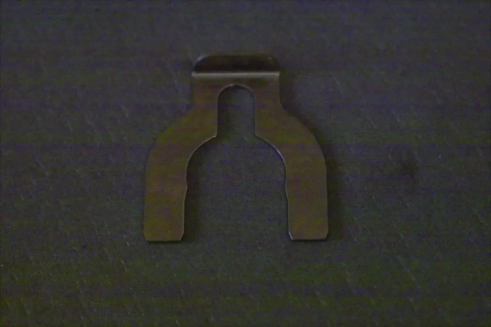 Metallclip in Form eines 3-Wege-Ventils, passend für Brötje Produkte, auf dunklem Hintergrund liegend.