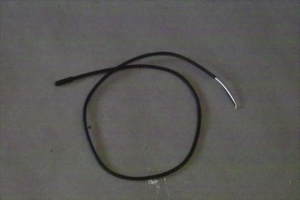 Schwarzes Kabel mit einem silbernen Ende, möglicherweise ein Temperaturfühler von Brötje, liegt auf einer grauen Oberfläche.