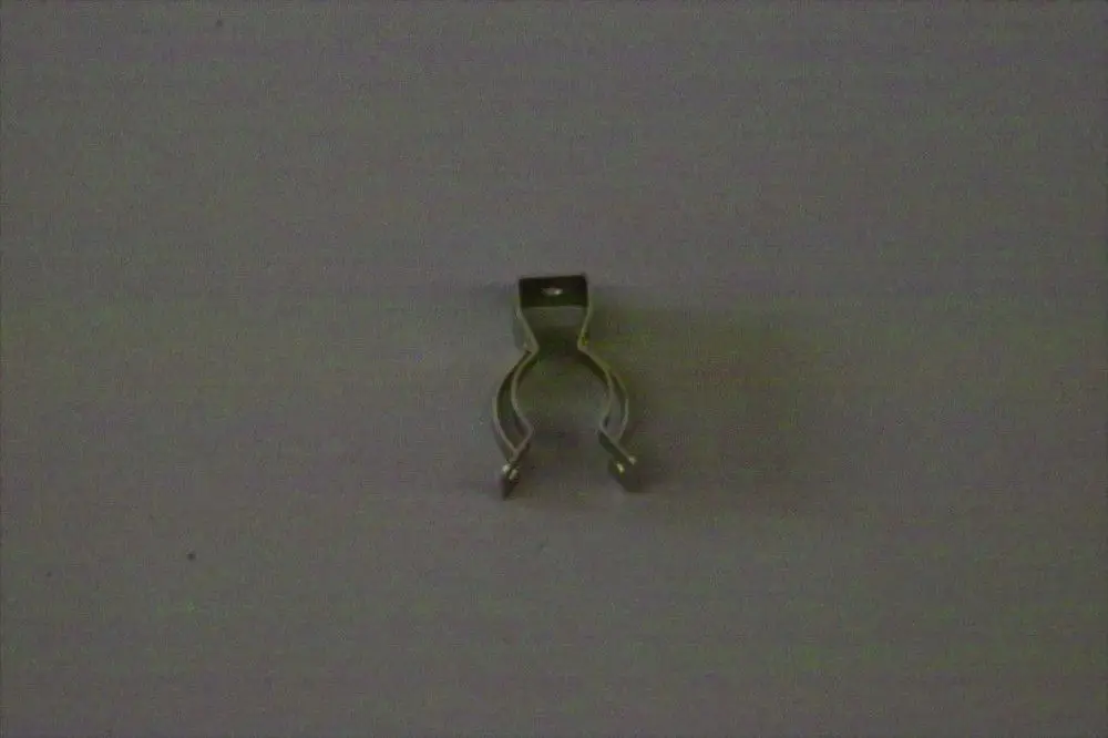 Brötje Arretierclip in metallischer Ausführung, mit zwei gebogenen Haltefüßen und einer oberen Verankerung, abgestellt auf einer neutralen Oberfläche.