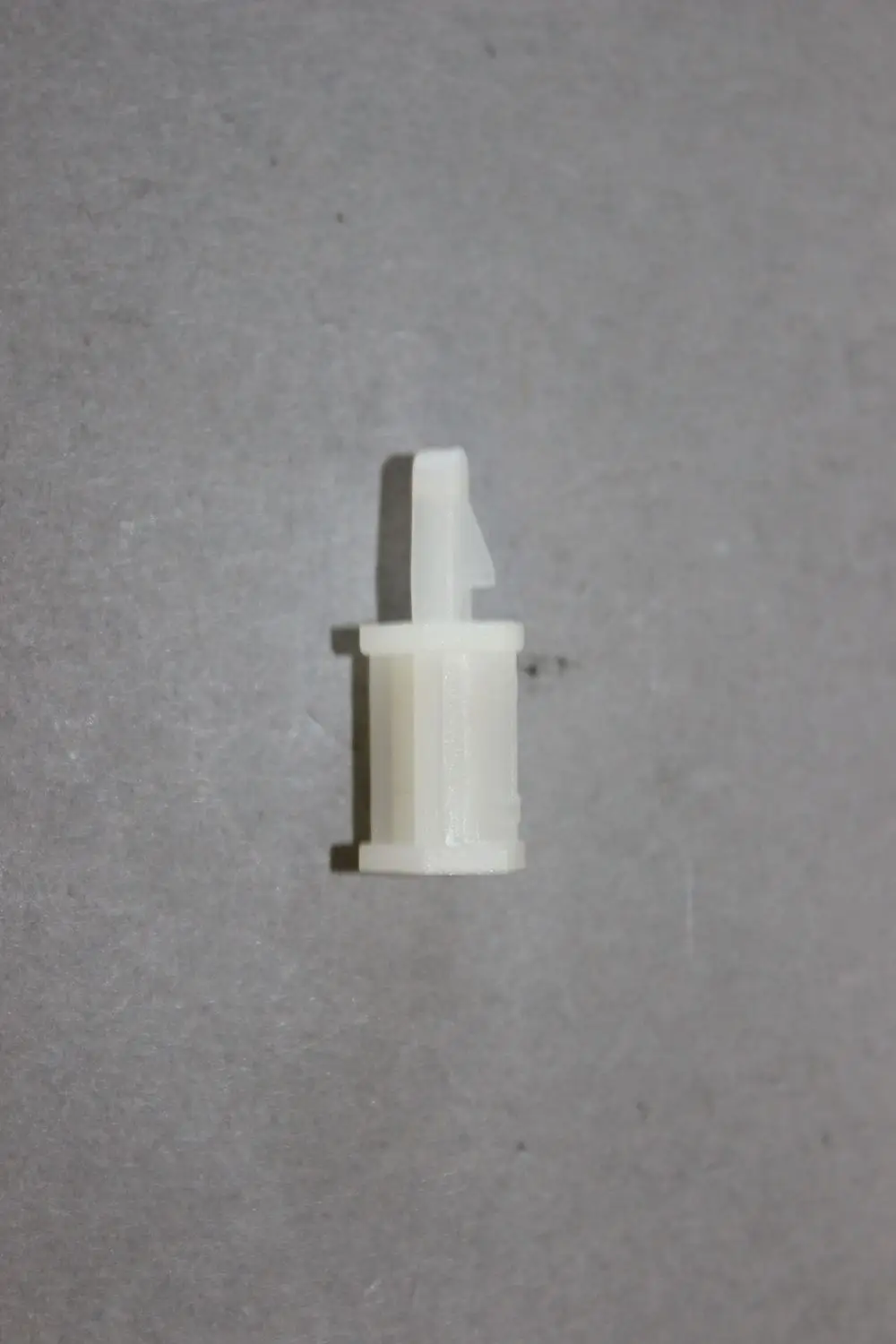 Kunststoffhalter von Brötje, zylindrische Form mit einem seitlichen Clip, auf grauem Untergrund.