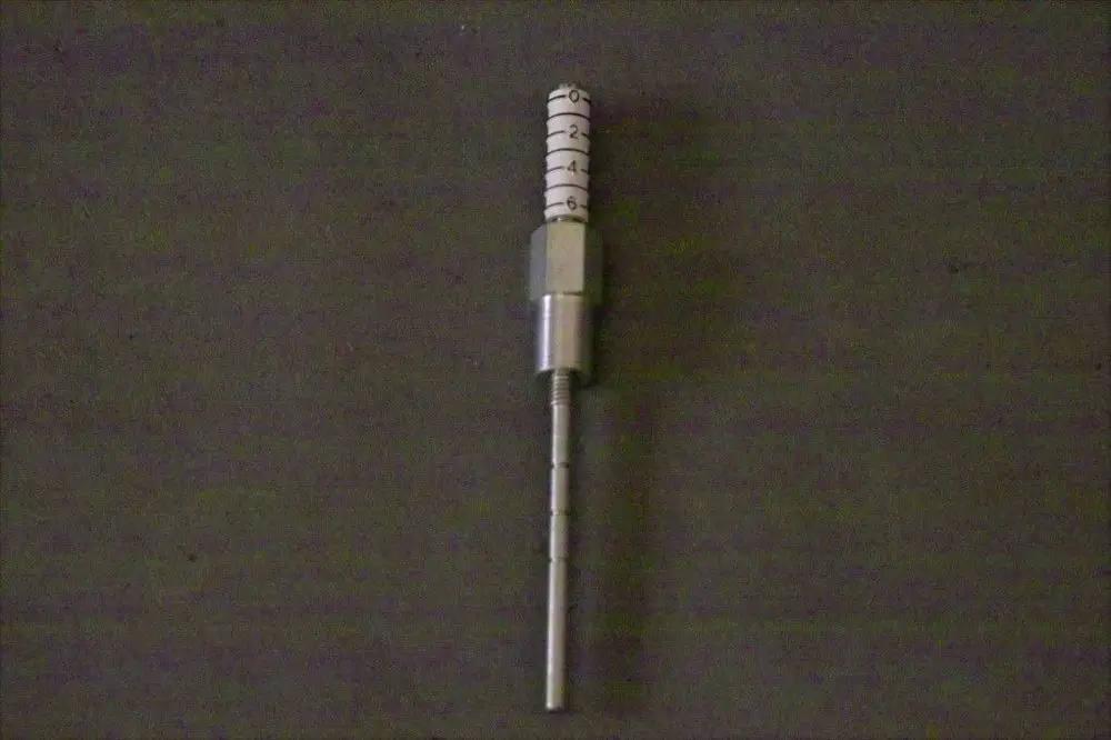 Brötje Luftklappenregelsystem mit senkrechtem Metallkörper, einer Skala am oberen Teil und einem feinen Stab für die Regelung, auf einem dunklen Hintergrund.