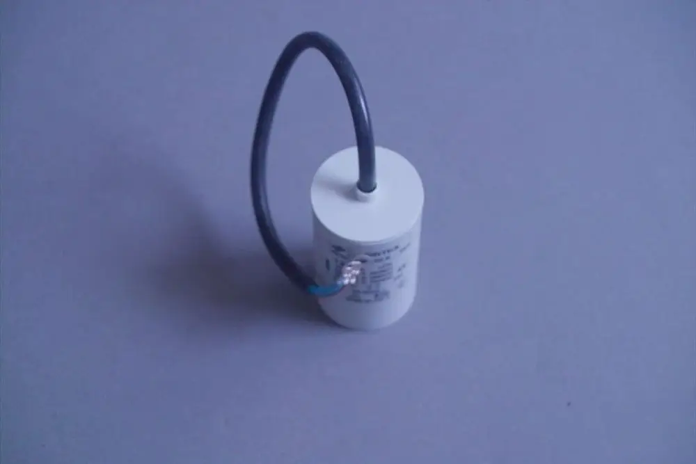 Weißer zylindrischer Brötje-Kondensator mit einem schwarzen Kabel, das oben befestigt ist, auf grauem Hintergrund.