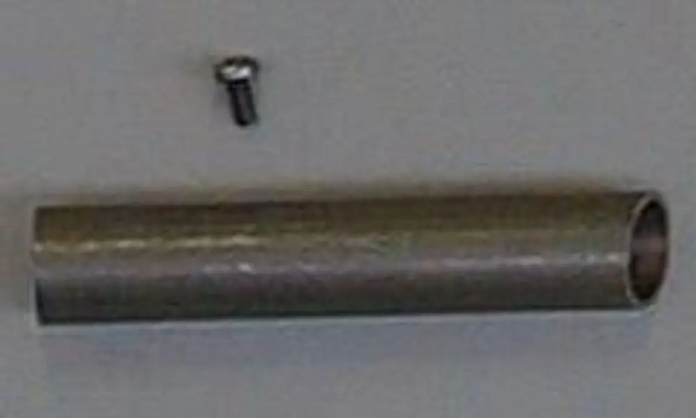 Rohr von Brötje mit einer metallischen Oberfläche, zylindrisch und lang, neben einer kleinen Schraube auf einem neutralen Hintergrund.