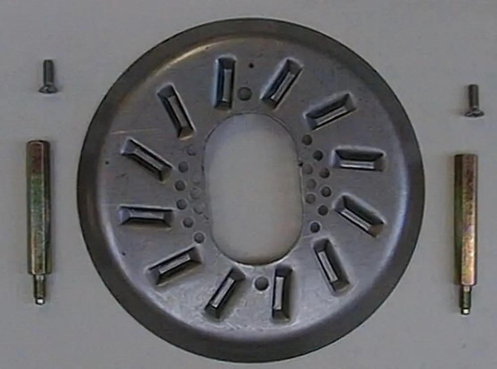 Brötje Stauscheibe, runde Metallplatte mit mehreren Aussparungen und Löchern, begleitet von zwei Befestigungsstiften und einer Schraube auf hellem Untergrund.