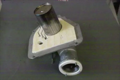Brötje Brennerkomponente mit einem runden Gehäuse und einem cylindrischen Behälter oben, montiert auf einer flachen Grundplatte.