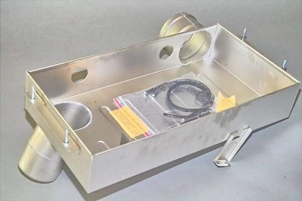 Aluminiumgehäuse mit mehreren Öffnungen und angeschlossenen Leitungen. Zubehörteile in einer Tüte im Inneren. Teil einer Brötje-Anlage zur Wärmeübertragung.
