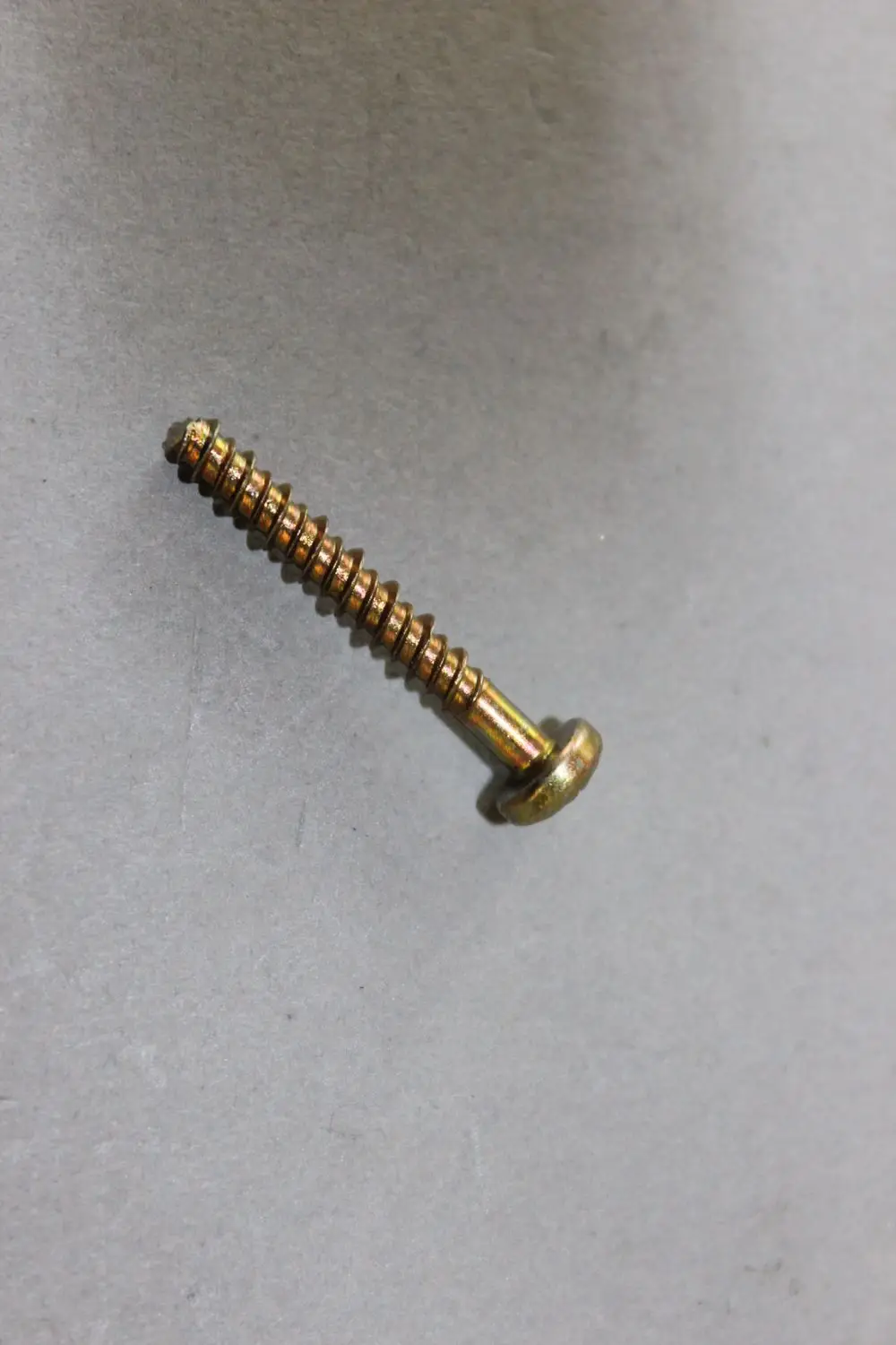 Brötje Linsenkopf-Schraube mit Kreuzschlitz, aus Metall, auf grauem Hintergrund. Die Schraube ist senkrecht auf dem Bild positioniert.