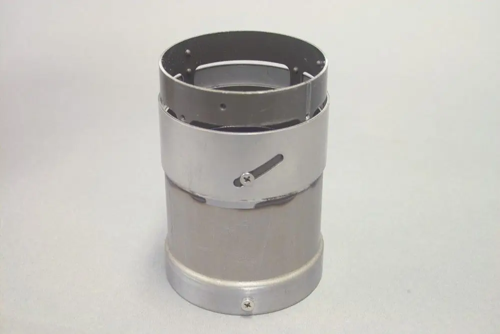 Brötje Flammenrohr in zylindrischer Form aus Metall mit verstellbarem Band, das den Umfang fixiert. Oberfläche ist unbeschichtet und zeigt dezente Spuren von Nutzung.