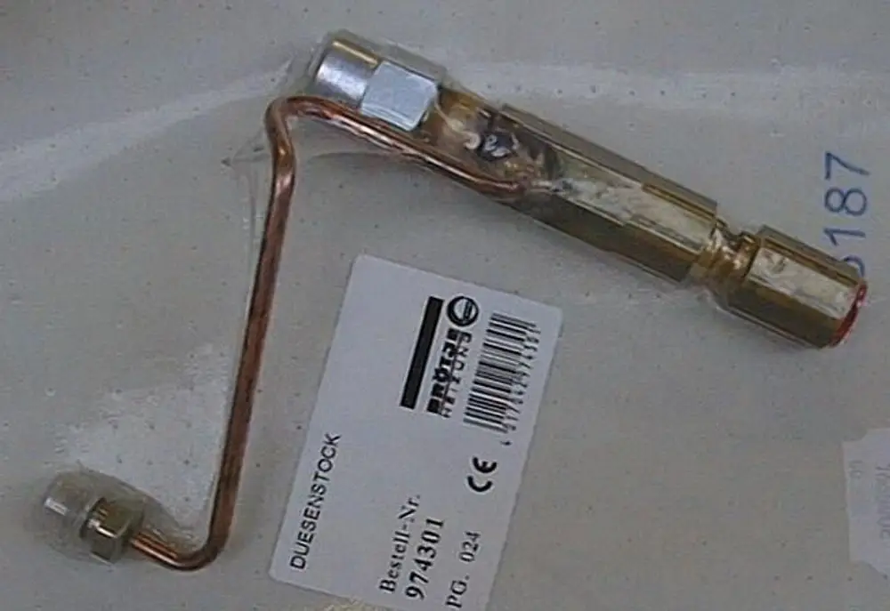 Brötje Düsenstock mit metallischem Gehäuse und geschwungener Kupferleitung. Sichtbar sind Anschluss- und Befestigungsteile.