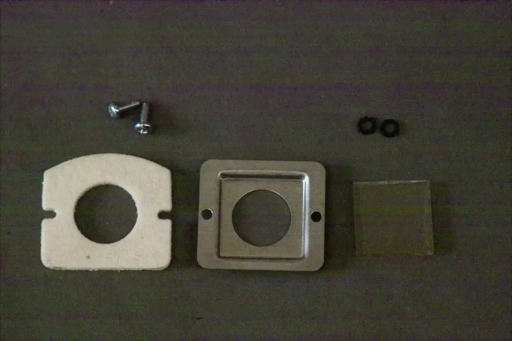 Brötje Schauglas-Set mit einer runden Dichtung, quadratischem Metallrahmen, einer transparenten Abdeckung und zwei Schrauben, alles auf einem dunklen Untergrund.